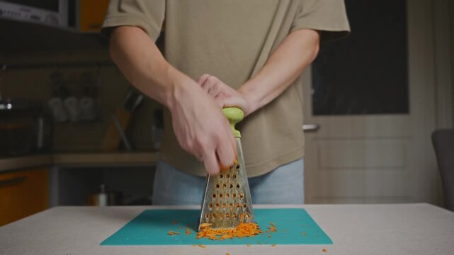 Close-up shot of hands grating a carrot on a metal kitchen grater. Detailed vegetable processing, food texture and everyday domestic cooking routine. High quality 4k footage