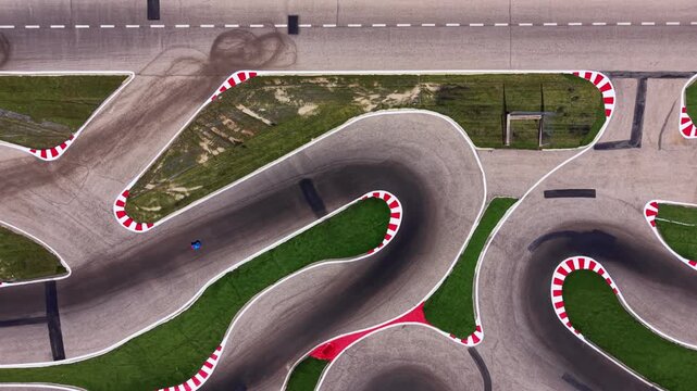 Top-down aerial view of radio controlled cars racing on a technical autodrome, highlighting tight chicanes, curbs, tire marks, and precise racing lines