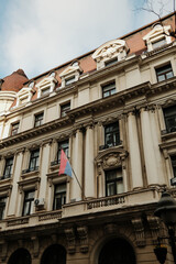 Fototapeta premium Grand neoclassical facade with columns and Serbian flag in Belgrade city center, highlighting official architecture and national identity in an urban setting.