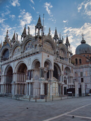 Fototapeta premium St Mark's Basilica Facade and Mosaics - Wide, majestic view of the ornate Byzantine facade of St. Mark's Basilica with marble arches, detailed mosaics, and spires under a cloudy blue sky.