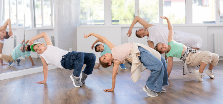 Emotional tween girl mastering krump dance routines during lively group session in children dance studio, guided by passionate male teacher..