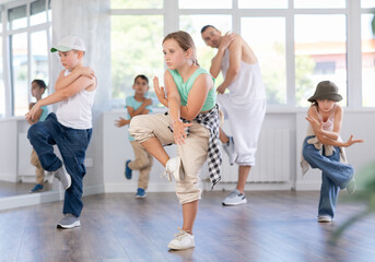 Fototapeta premium Young girl and group of positive children practicing energetic hip hop movements at modern dance school