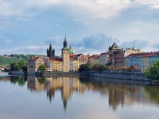Obraz premium Vltava River Prague Panorama Sunny Day - Scenic view of the Vltava River, historical buildings, and green trees under a bright blue sky.