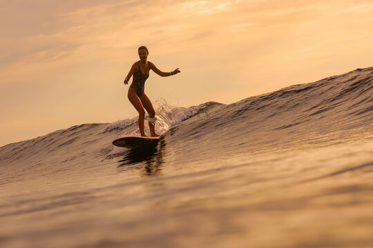 Sunset Woman Surfing On Longboard Riding Smooth Crest, Warm Golden Light, Calm Balance And Relaxed Stance