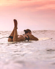 Young Woman Resting On Surfboard In Calm Sea, Legs Raised And Relaxed, Scanning Soft Clouded Horizon, Patient