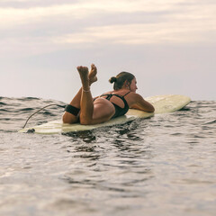 Young Woman Resting On Surfboard During Sunset Lull, Legs Playfully Raised, Soft Waves And Warm Sky, Mellow
