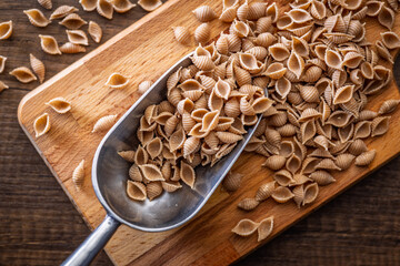 Wholegrain conchiglie pasta on scoop on wooden table. Top view.