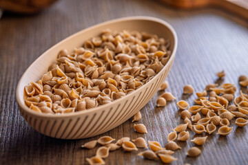 Wholegrain conchiglie pasta in bowl on wooden table.