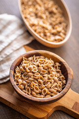 Wholegrain conchiglie pasta in bowl on wooden table.
