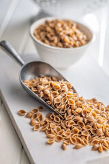 Wholegrain conchiglie pasta in scoop on white table.