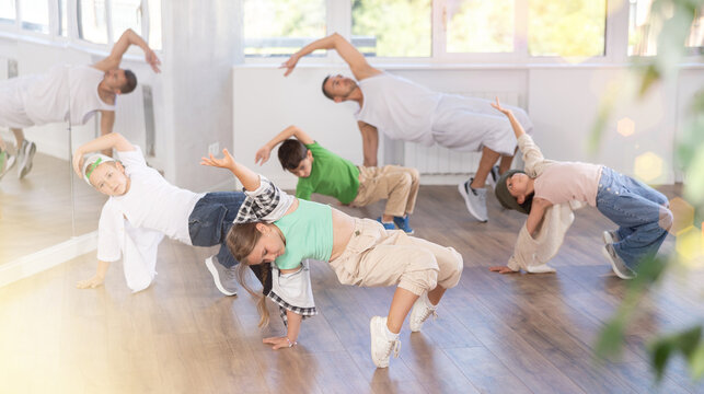 Emotional tween girl dancer rehearsing modern krump dance moves during group workout in kids studio under guidance of male instructor