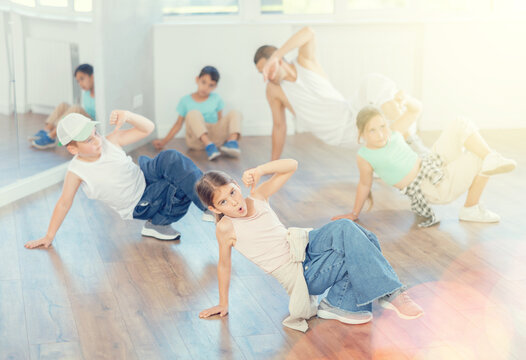 Smiling sports teen girl performing krump movements on floor with group children in modern breakdance studio with male coach