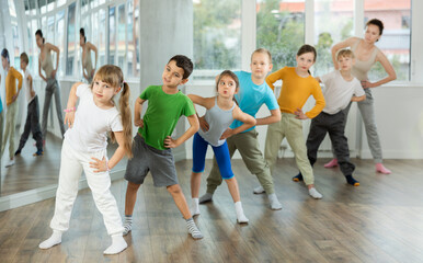 Positive preteen children engaged in choreography exercises together with trainer in training room