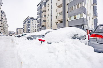 Fototapeta premium Red snow brush sticking out of deep snow covering parked cars in residential courtyard after heavy winter blizzard in the city