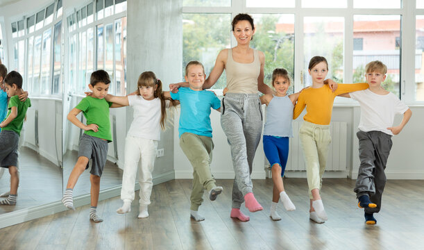 Positive preteen children learning to dancing folk dance in row in studio