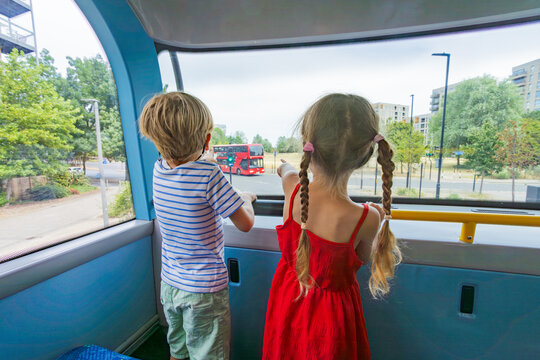 Two kids excitedly point at a red imperial bus from upper deck