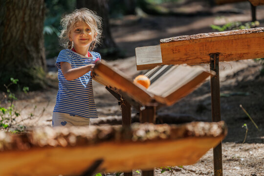Cute girl playing with wooden marble run path in a sunny forest