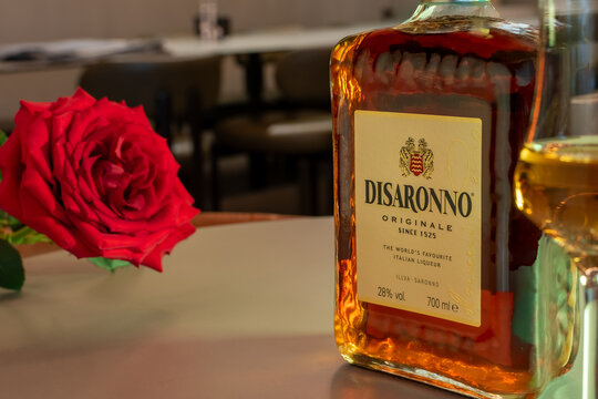 Bottle of Disaronno Originale amaretto liqueur with blooming red rose on a cafe table. Professional lifestyle photography with soft ambient lighting. Ukraine, Zhytomyr, February 23, 2026