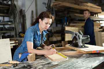Work in woodworking enterprise - woman measures length of wooden board with a tape measure