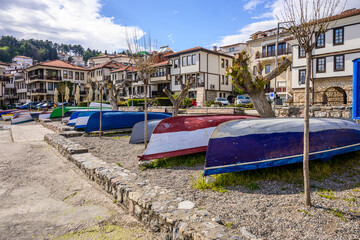A row of weathered, brightly painted fishing boats are overturned on a pebble-strewn shore,...