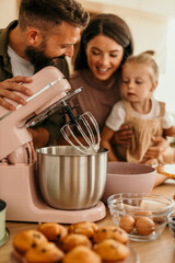 Family baking muffins together in kitchen with mixer