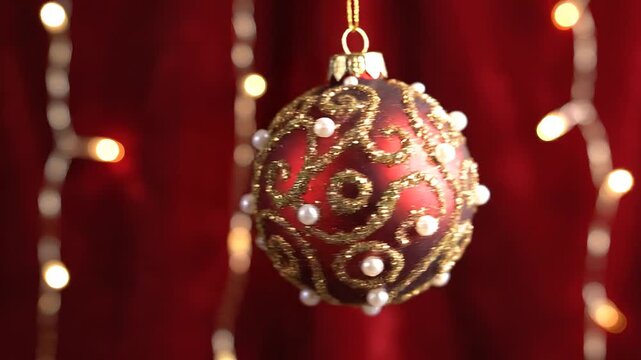 Decorative christmas ornament hanging in front of red velvet curtains with warm string lights in the background, used for holiday greeting or festive decoration