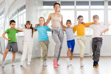 Fototapeta premium Positive preteen children doing cancan dance together with female trainer in dancing studio