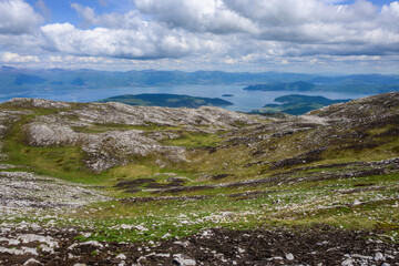 Fototapeta premium An expansive view descending into a verdant, rocky mountain valley within Galicica National Park, culminating in the serene blue waters and distant shores of Lake Prespa.