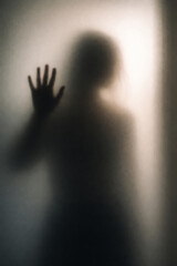 Verschwommene Silhouette einer Frau hinter Milchglas mit erhobener Hand