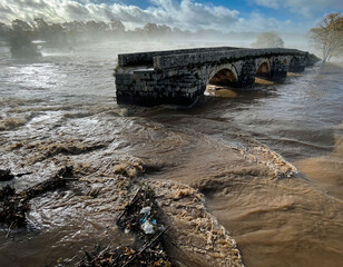Damaged stone bridge over flooded river with turbulent water