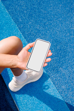 Hand Holding phone with White Screen Mockup on a blue athletic surface