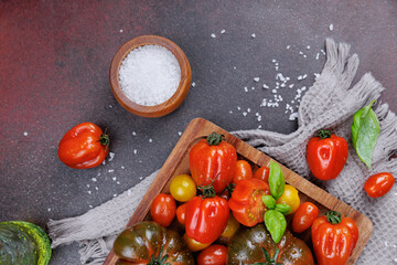 Flat lay of fresh cherry and heirloom tomatoes with basil leaves, salt, and textured towel on rustic kitchen surface, promoting healthy vegetarian meals
