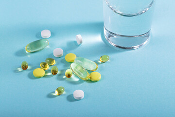 Diet, nutrition, healthy eating concept. Assorted pharmaceutical medicine pills, tablets and capsules and glass of water for pouring over blue background