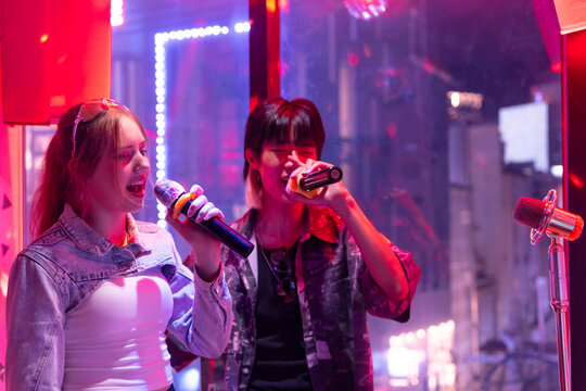 Two Friends Singing Karaoke at a Lively Venue in the Evening