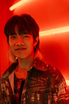 Young Man Asian Stands in Vibrant Red Light With Neon Backdrop
