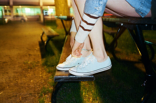 Woman trying her shoe sitting on a park bench at night. 