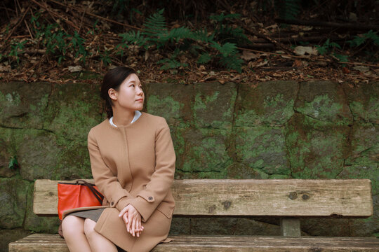 Asian Woman in a Camel Coat on a Wooden Bench.