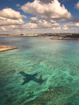 Airplane shadow over crystal clear turquoise water in Okinawa, Japan, symbolizing travel and tropical vacation