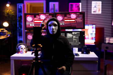 Fototapeta premium Hacker group cybercriminal wearing anonymous mask filming video threatening another country government to steal military secrets, doing international espionage in underground secret hideout