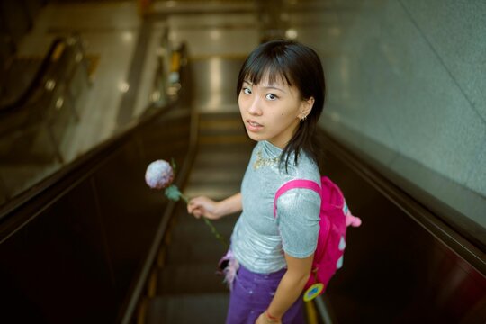 Girl Going Down Escalator With a Flower in a Busy Urban Area