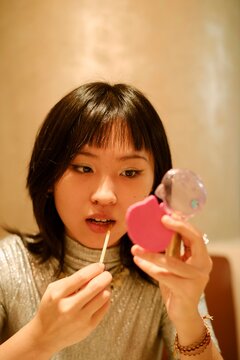 Young Woman Applying Lip Gloss in a Stylish Setting