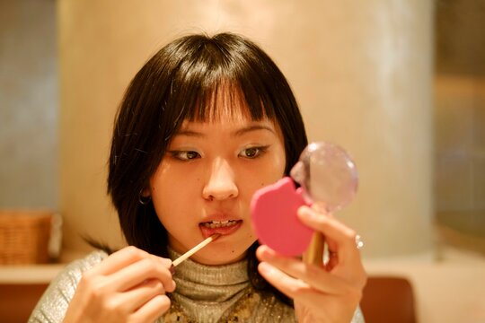 Young Woman Applying Lip Gloss at a Cozy Cafe in the Evening