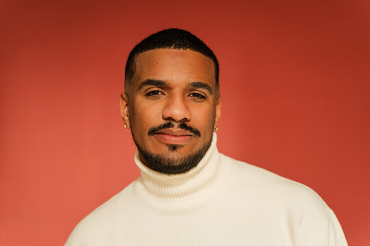 Smiling man stands against red studio background