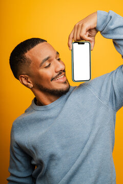 Smiling man holds mobile phone with blank creen in studio