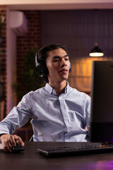 Male entrepreneur using wireless headset while reading emails and working on computer. Modern remote worker enjoying music for concentration and managing projects in apartment office.