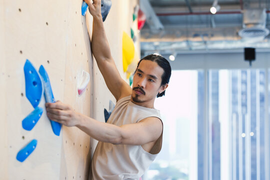 Asian Climber On Indoor Rock Wall Reaching For Holds