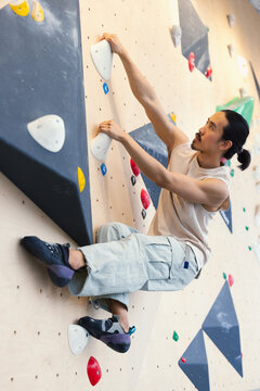 Climber On Indoor Wall Holds On, Focused While Climbing