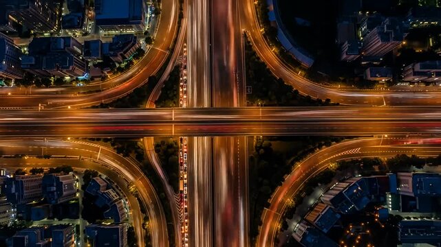 Aerial view of a glowing highway interchange at night, surrounded by buildings