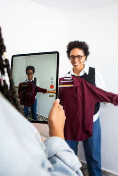 Young women using tablet to show second hand clothing. 