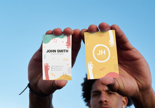Real photo of front and back business cards held up by man. PSD mockup